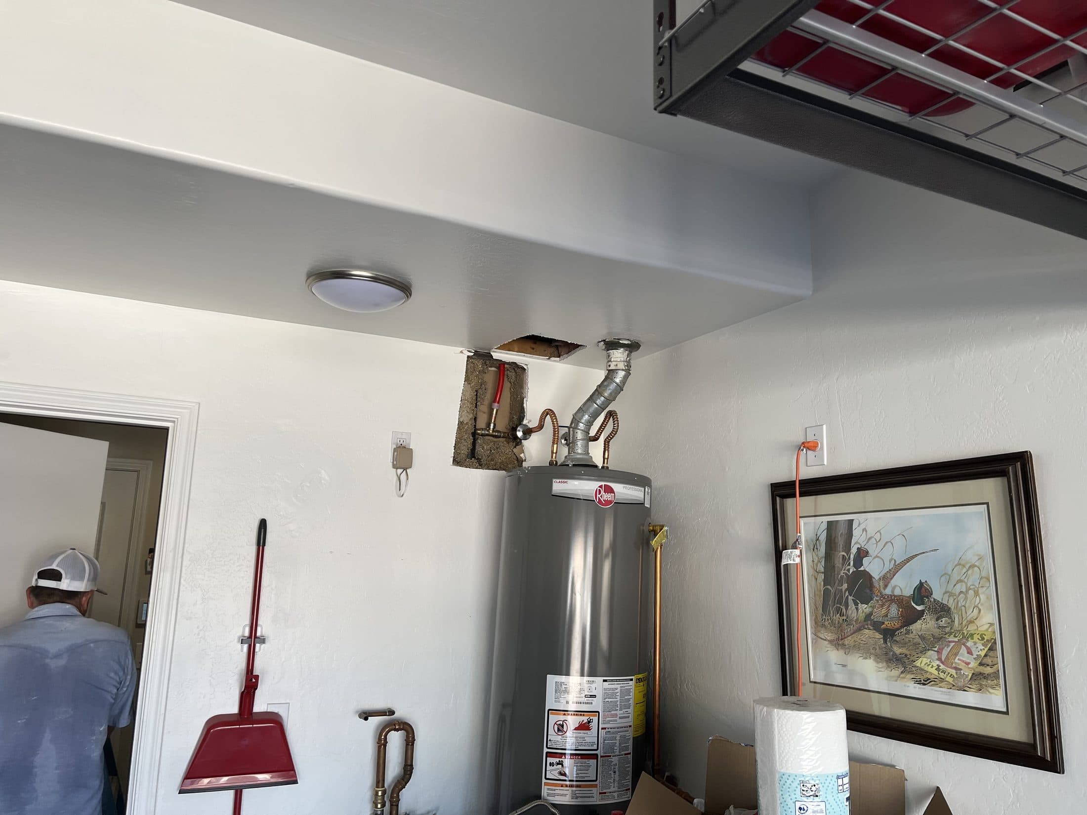 Garage ceiling opened during a slab leak reroute, with a new water line dropped down the wall cavity to the water heater